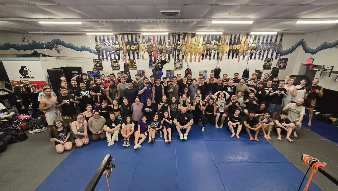 TCB athletes gathered on the gym floor beneath a display of belts.